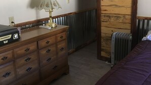 Et soveværelse med en trækommode, en lampe, en radiator og en seng med lilla dyne.