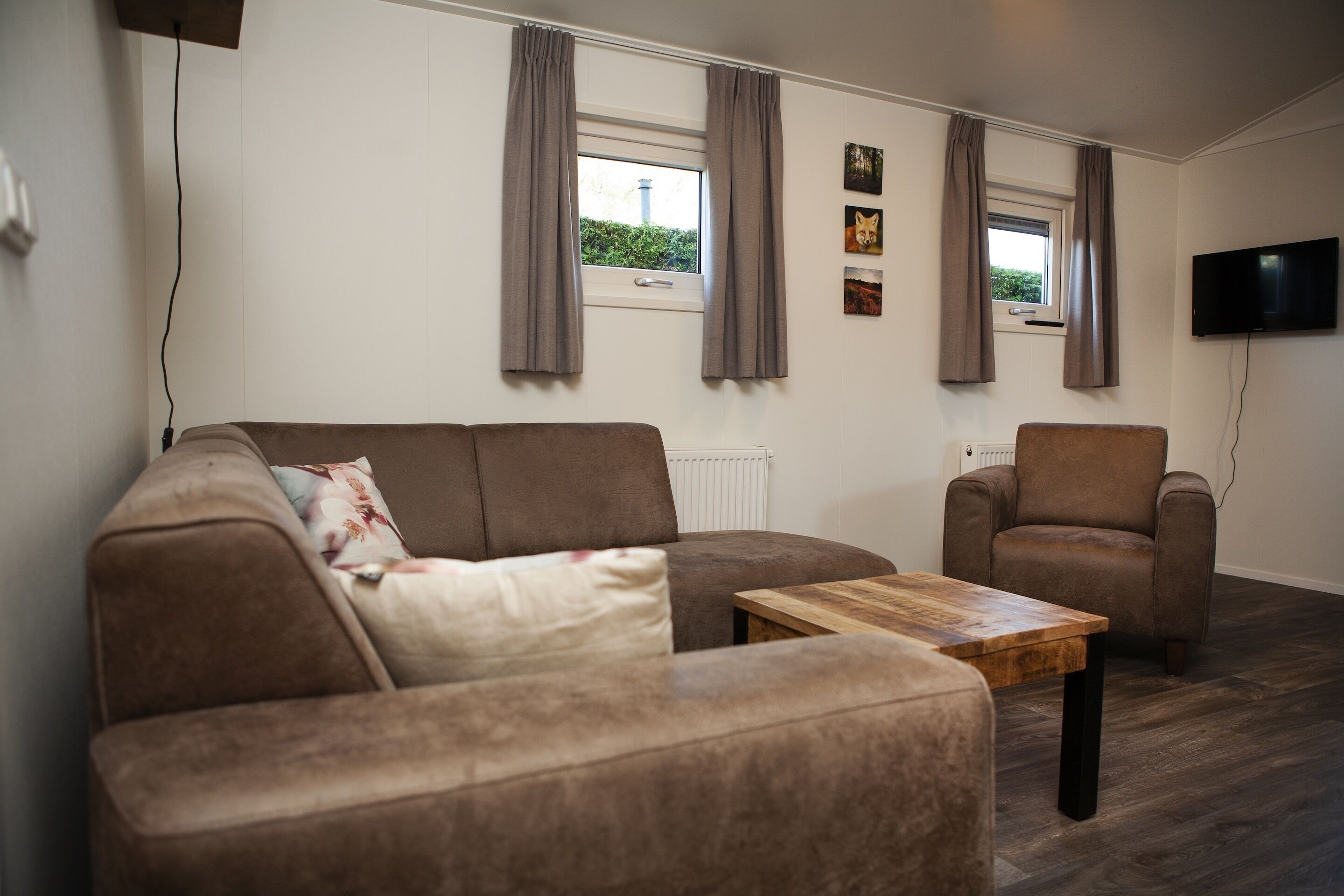 Un salon avec un canapé marron, une table basse en bois, un fauteuil marron et un téléviseur fixé au mur.