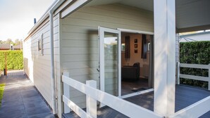A house with a covered porch, a sliding glass door leading to a room with a chair and a table, and a neatly trimmed hedge in the background.