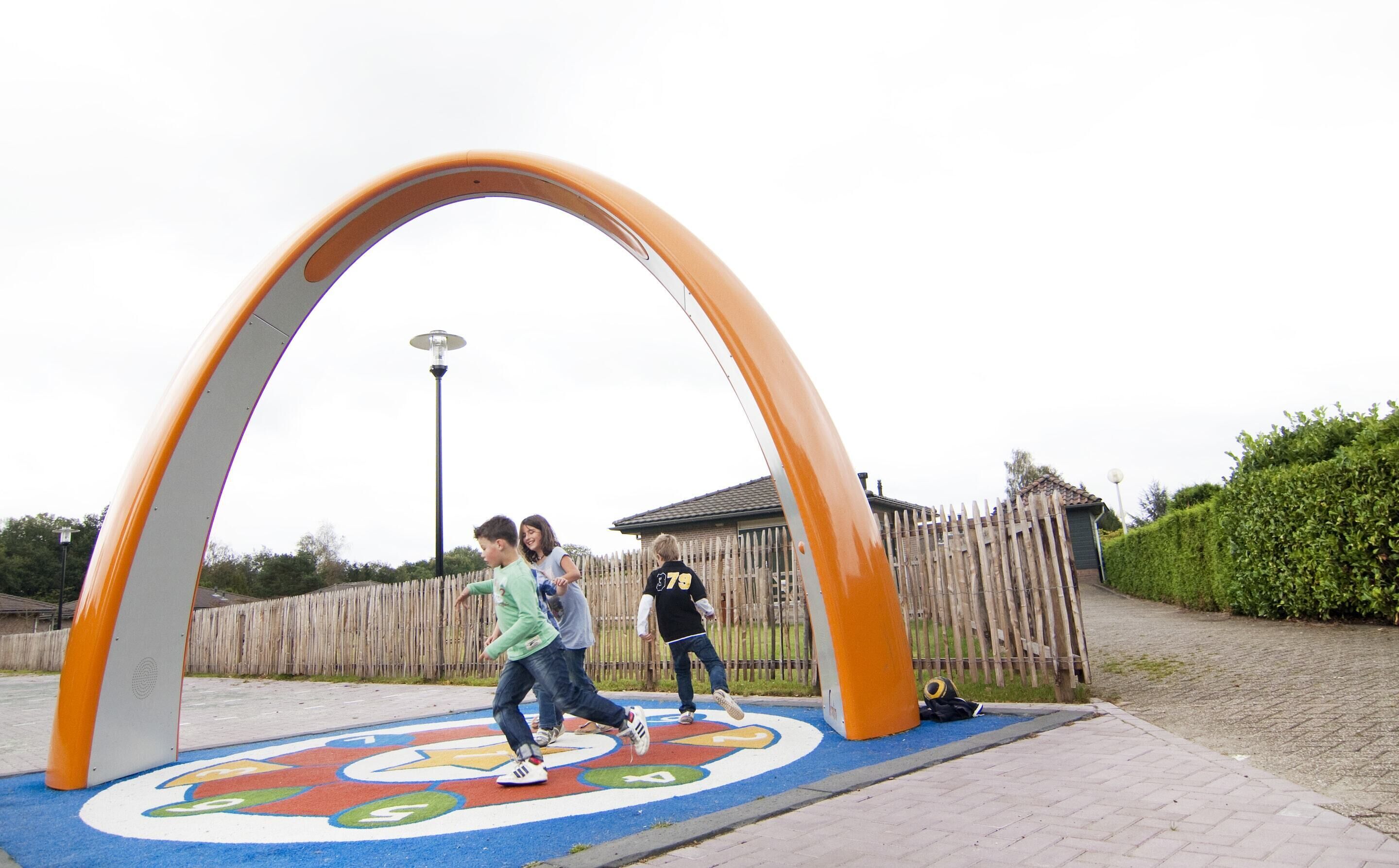 Kinderen spelen op een kleurrijke speeltuin met een grote bogenconstructie.