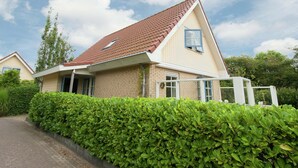 A two-story house with a red-tiled roof, beige walls, and a brick foundation. - Holiday Home in Schoorl with Fenced Garden near Dunes (Schoorl)