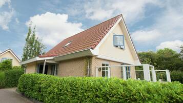 A two-story house with a red-tiled roof, beige walls, and a brick foundation.