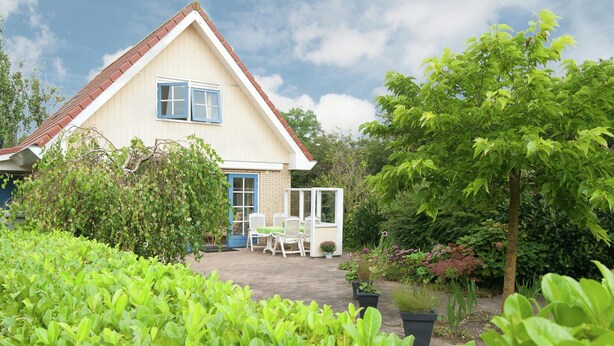 A house with a white exterior and a red roof, surrounded by lush greenery and a garden. - Holiday Home in Schoorl with Fenced Garden near Dunes (Schoorl)