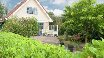 A house with a white exterior and a red roof, surrounded by lush greenery and a garden.