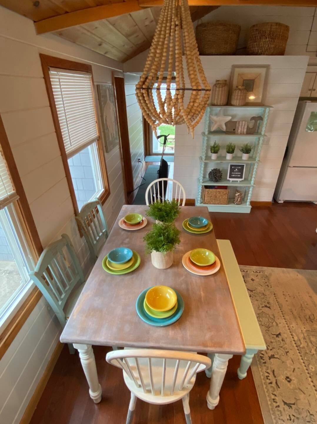 Comedor con mesa de madera, sillas blancas y platos coloridos.