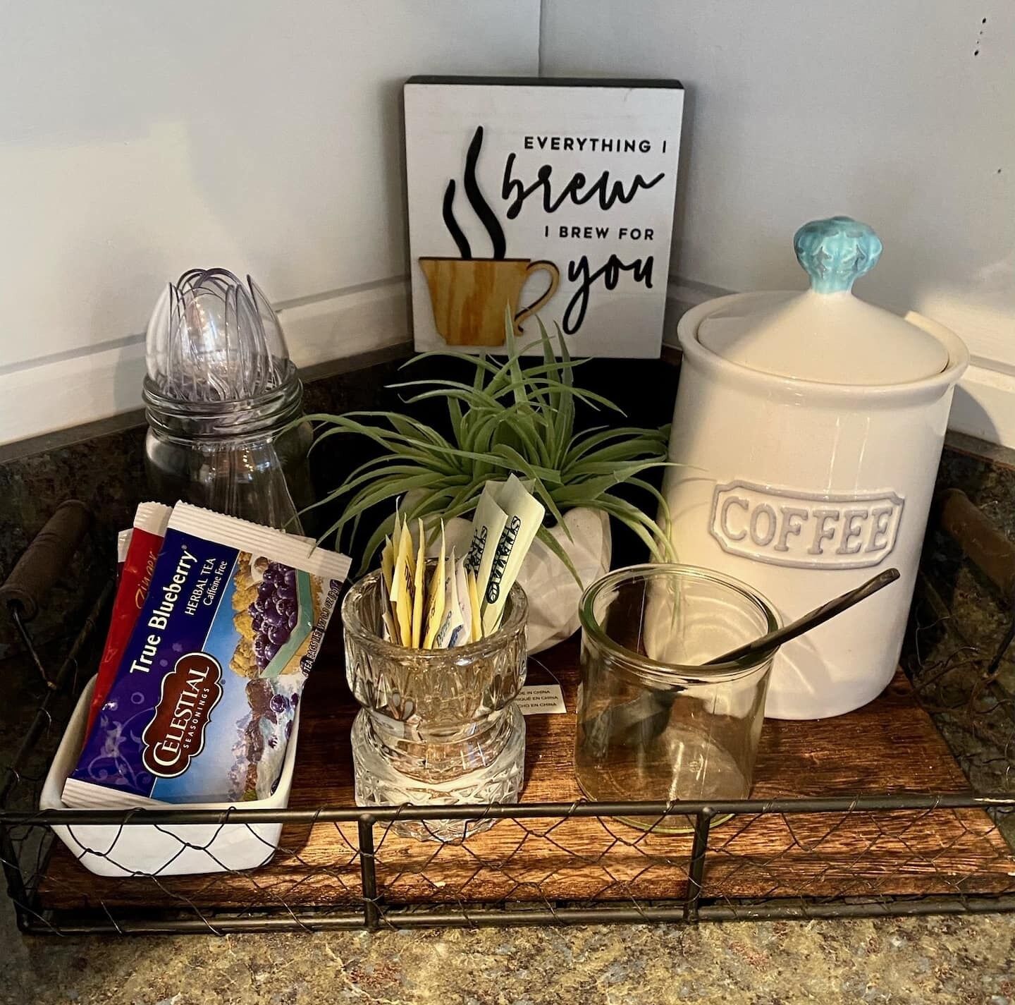 Una encimera de cocina con una cafetera, un tarro de granos de café, un sobre de té, una planta y un letrero que dice 'Everything I brew for you'.