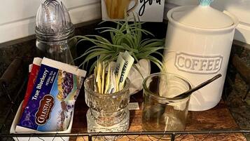 Una encimera de cocina con una cafetera, un tarro de granos de café, un sobre de té, una planta y un letrero que dice 'Everything I brew for you'.