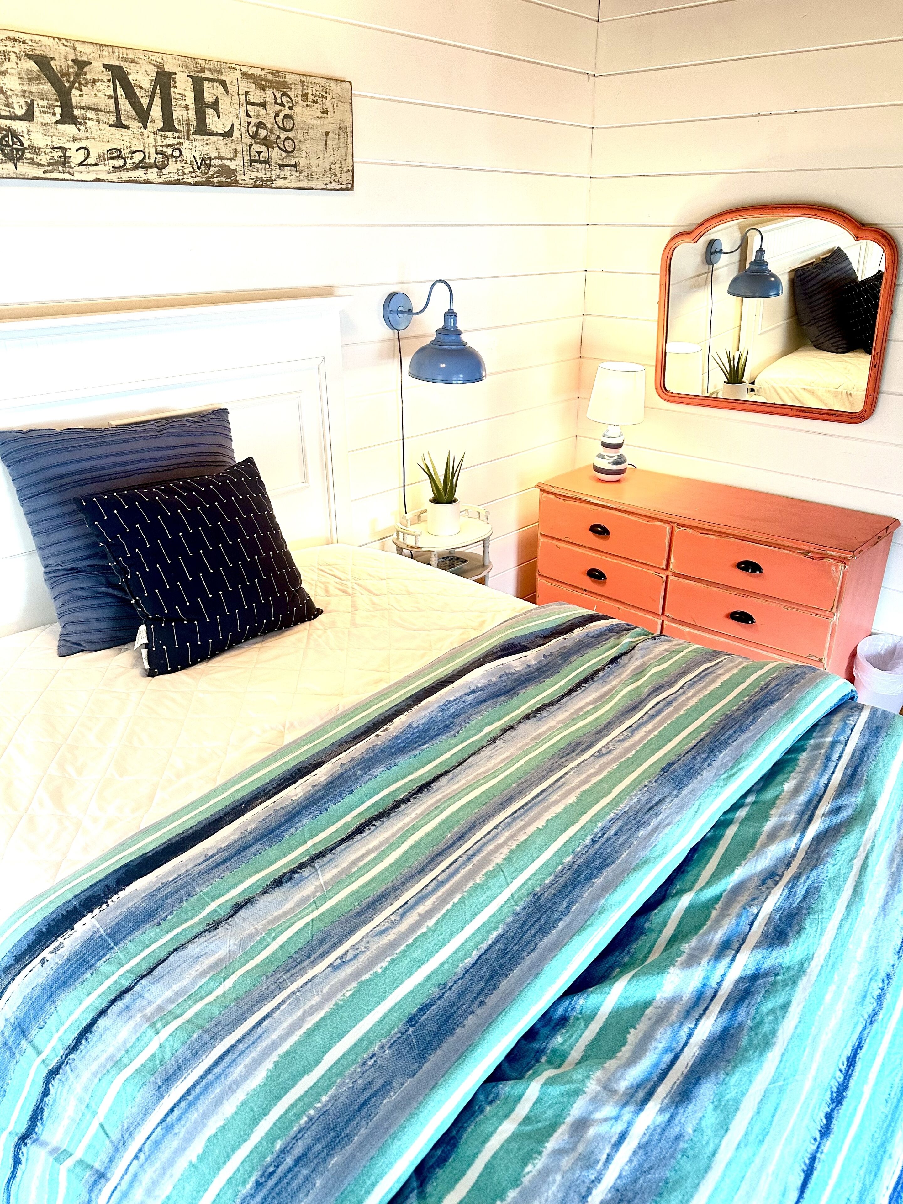 A bedroom with a bed, a dresser, a mirror, a lamp, and a wall-mounted sign.