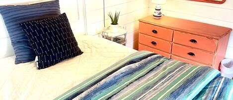 A bedroom with a bed, a dresser, a mirror, a lamp, and a wall-mounted sign.