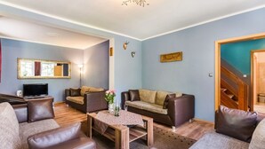 Una sala de estar con sofás de cuero, una mesa de centro de madera, un televisor de pantalla plana y una lámpara decorativa en el techo.