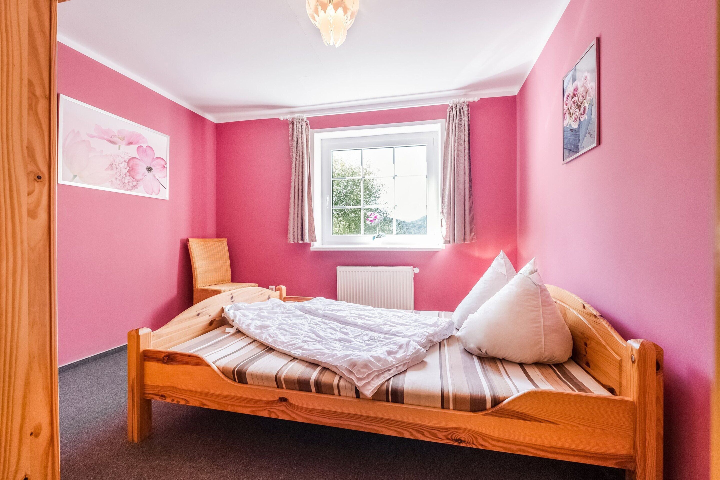 Et soveværelse med en træseng, pink vægge, et vindue med gardiner og en radiator.