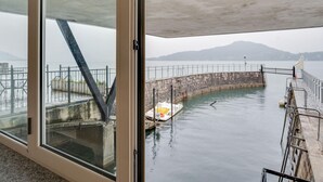 A view from inside a building looking out to a body of water with a stone pier and a small boat. - Holiday Home in Meina With Private Beach (Meina)