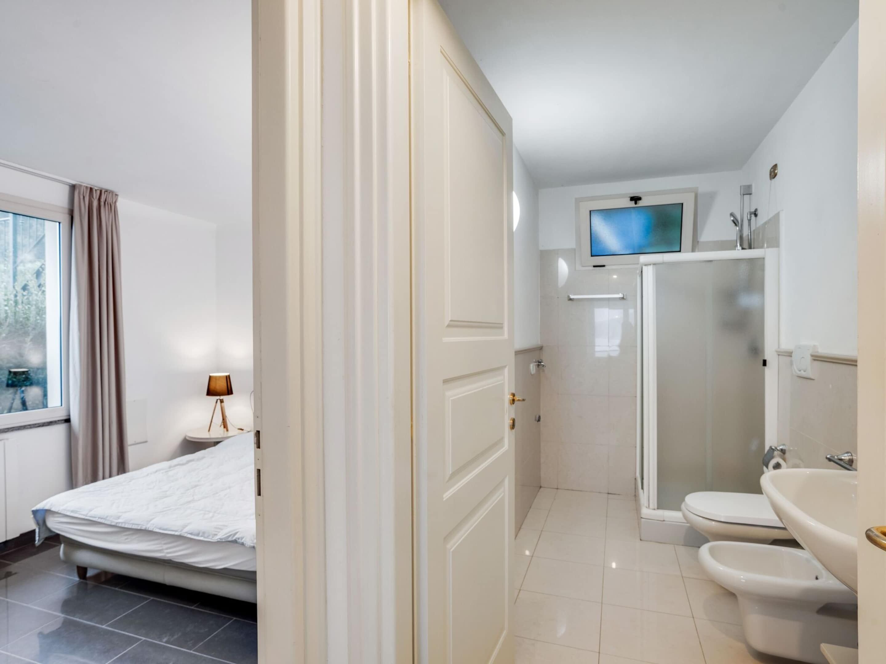 A hotel room with a bed, a desk with a lamp, a TV, a shower, and a toilet.