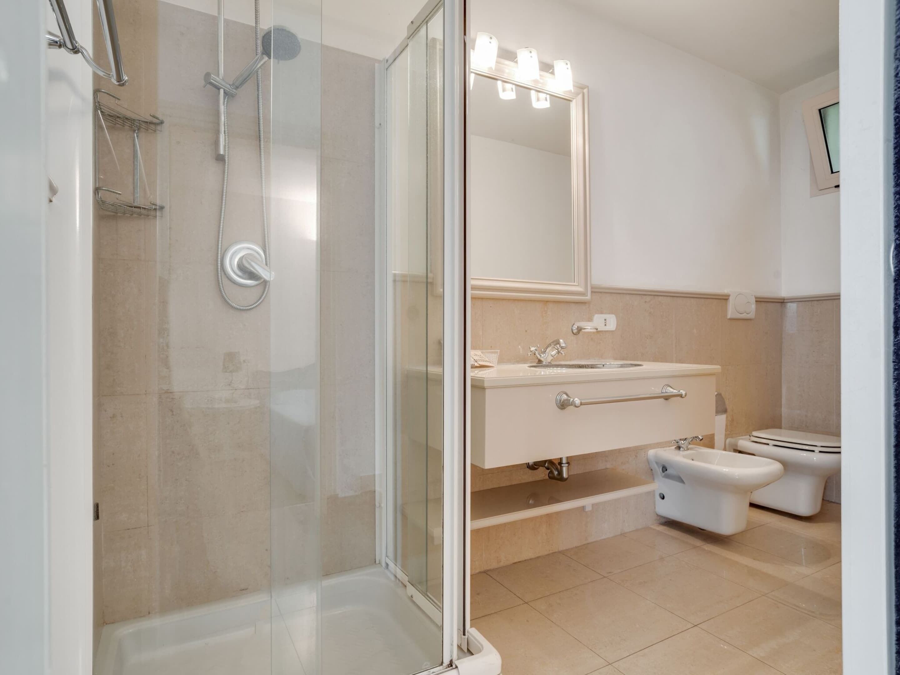 A modern bathroom with a glass-enclosed shower, a vanity with a sink and mirror, and two toilets.