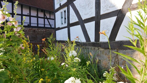 Ein traditionelles Fachwerkhäuschen mit Steinwand und Holzzaun.
