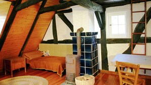 Ein gemütliches Schlafzimmer im Dachgeschoss mit schrägen Wänden, einem hölzernen Bett, einem kleinen Tisch und einem alten Kochherd.