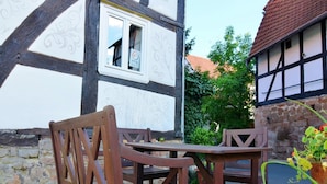 Ein traditionelles Fachwerkhäuschen mit steinernem Fundament und einem Holztisch und Stühlen davor.