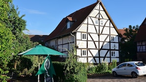 Ein traditionelles Fachwerkhäuschen mit geneigtem Dach, einem grünen Sonnenschirm und einem geparkten Auto davor.