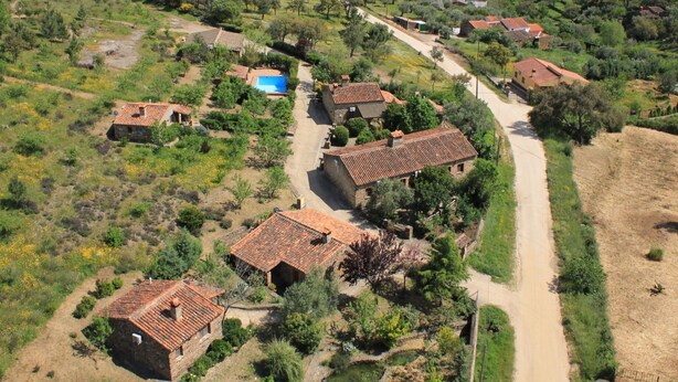 Luchtbeeld van een landelijk dorp met traditionele huizen met terracotta daken, een onverharde weg en verspreide begroeiing.