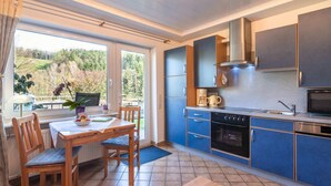 A modern kitchen with blue cabinets, a wooden dining table, and a view of the outdoors. - Apartment in the Odenwald With Terrace (Mossautal)