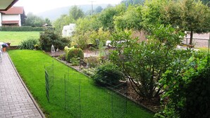 A garden with a paved walkway, a fenced area, and a variety of plants and trees. - Apartment in the Odenwald With Terrace (Mossautal)