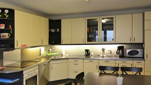 A compact kitchen with a microwave, coffee maker, and a sink. There are cabinets, a dining table with chairs, and a small oven. - Gruppenfreundliche Villa in Liesen (Hallenberg)