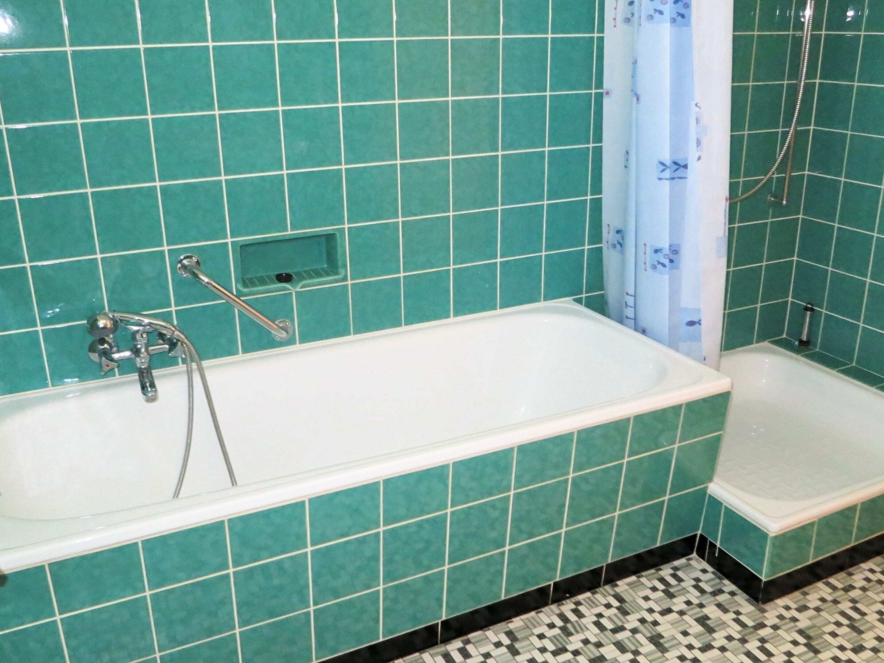 Een badkamer met een witte badkuip, douche en wastafel. De wandtegels zijn turquoise.