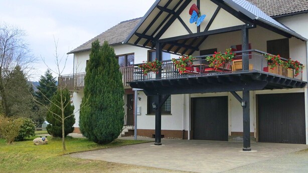 A two-story house with a balcony, a garage, and a large tree in the front yard. - Gruppenfreundliche Villa in Liesen (Hallenberg)