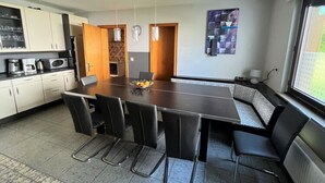 A modern kitchen with white cabinets, a dark countertop, and a dining area with a large table and black chairs. - Gruppenfreundliche Villa in Liesen (Hallenberg)