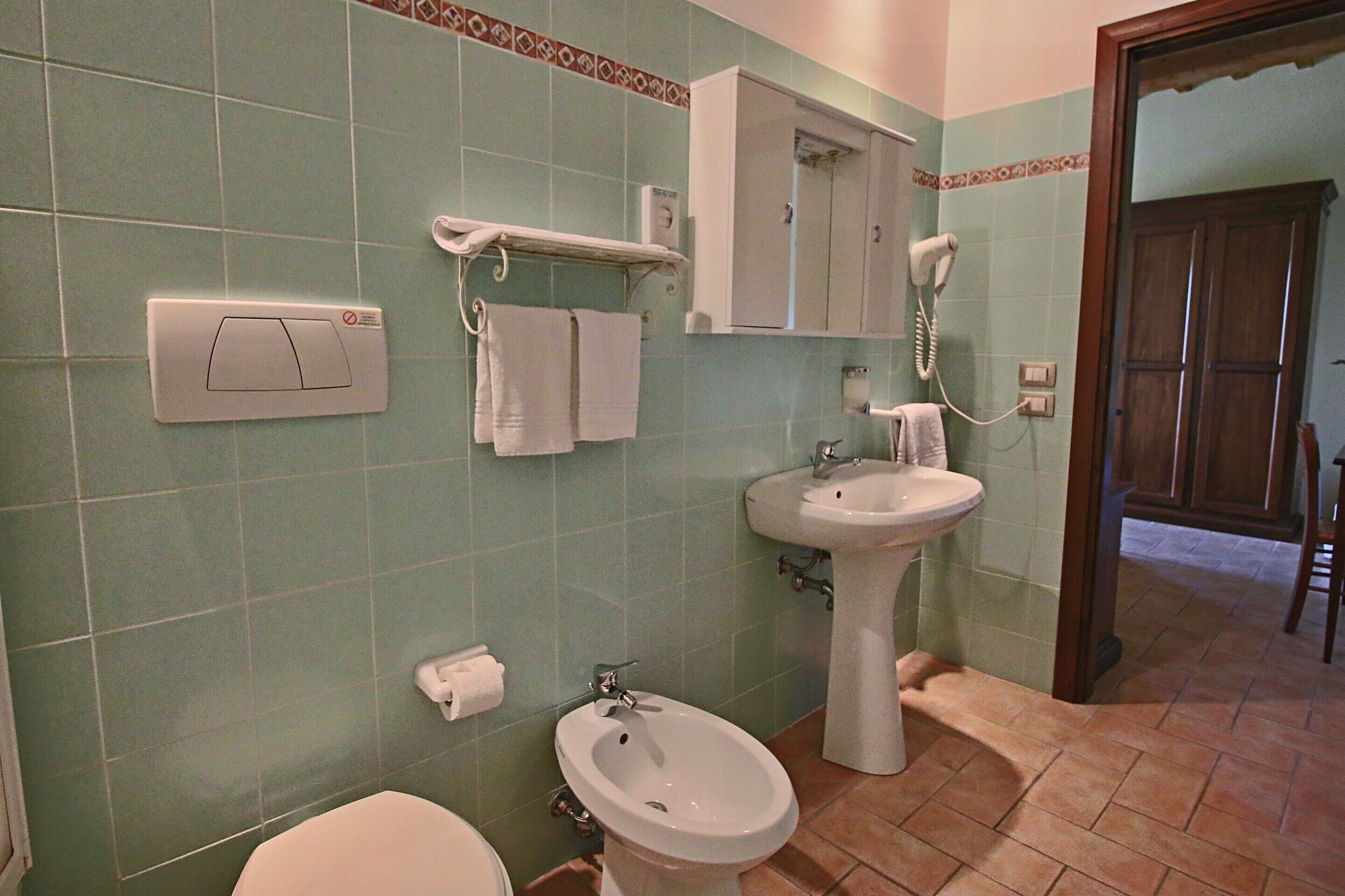 Un baño con inodoro, bidé, lavamanos, toallero y secador de pelo.