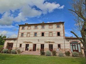 A two-story stone building with a symmetrical facade, multiple windows, and a central entrance with steps leading up to it. - Cottage in Urbania With Pool & Terrace (Urbania)