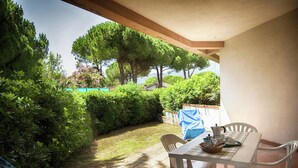 Une terrasse avec une table et des chaises, entourée de verdure et offrant une vue sur des arbres et une piscine.