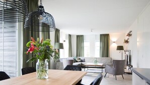 A modern living room with a wooden dining table, black chairs, a grey sofa, and a green vase with flowers. - Group Villa in Netherlands With Privacy (Voorthuizen)