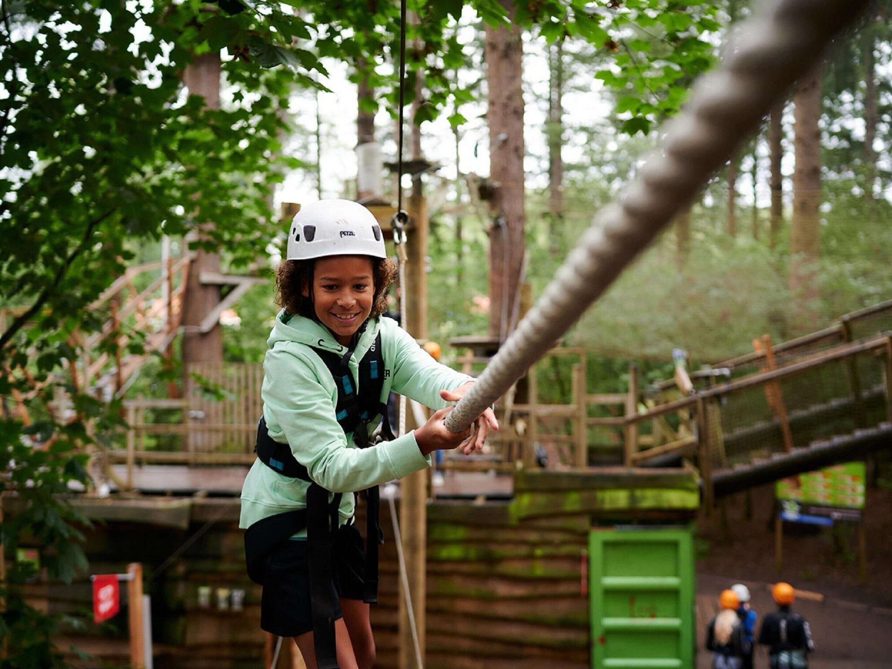 A person in a helmet and harness on a rope bridge in a wooded area.