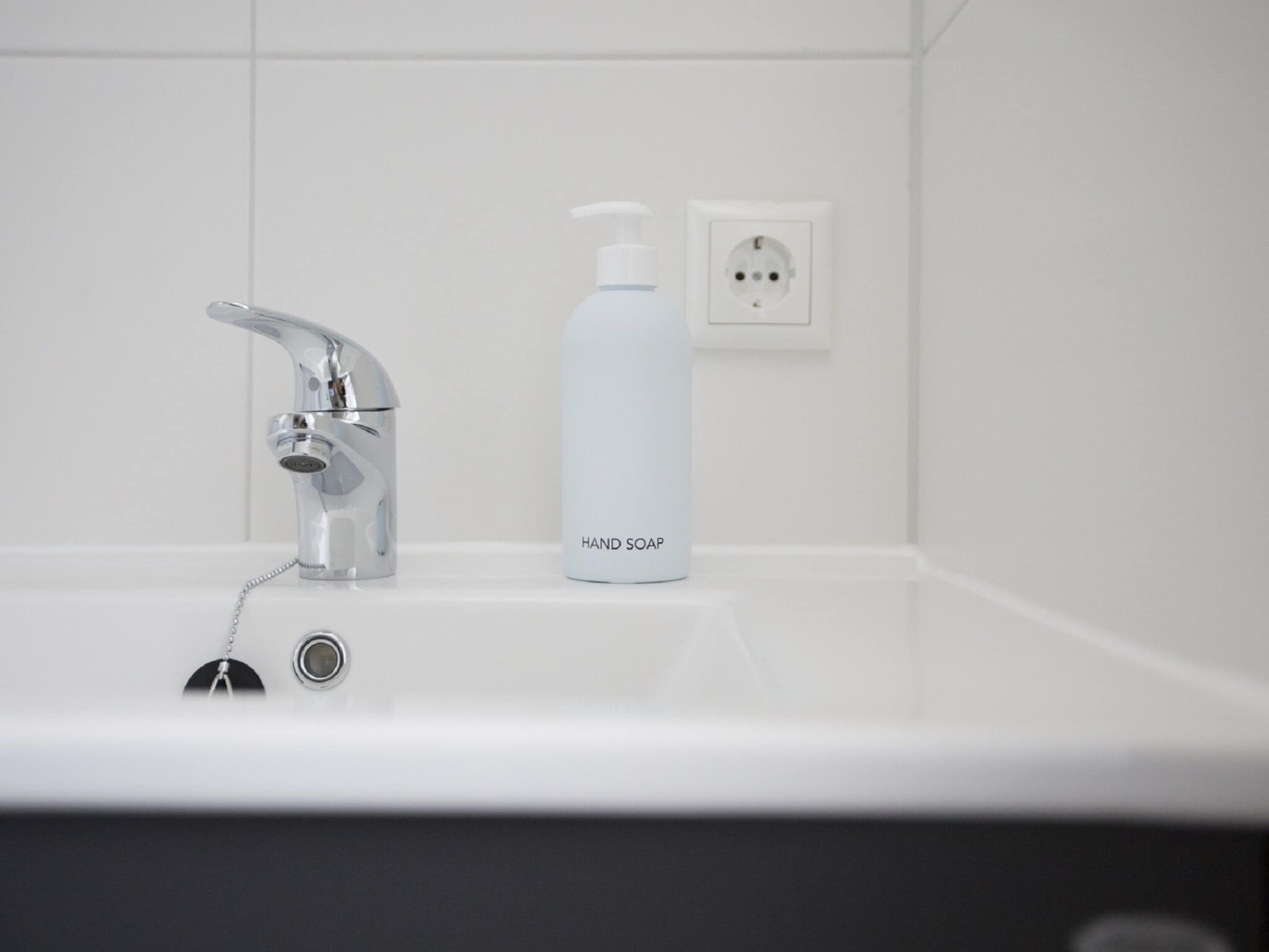 A bathroom with a modern sink, a hand soap dispenser, and a power outlet.