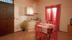 A compact kitchen with wooden cabinets, a tiled backsplash, a dining table set with red chairs, and a window with red curtains. - Farmhouse With a Magnificent Panorama, Swimming Pool, Near Cagli (Cagli)