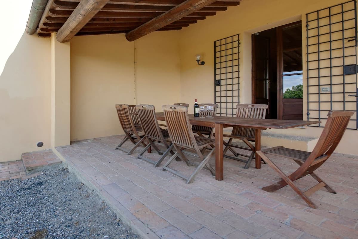 Eine Terrasse im Freien mit einem Holztisch und Stühlen, einer Weinflasche und einem Weinglas.