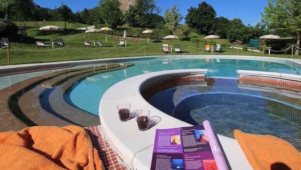 A pool area with a hot tub, lounge chairs, and a view of a hill with a building. - Apartment in Marche With Pool Access (Apecchio)