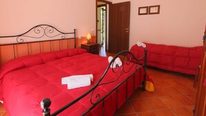 A bedroom with a large bed, a smaller bed, a nightstand with a lamp, and a door leading to another room. - Apartment in Marche With Pool Access (Apecchio)