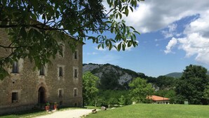 A stone building with multiple windows, a grassy area, and a mountain in the background. - Apartment in Marche With Pool Access (Apecchio)