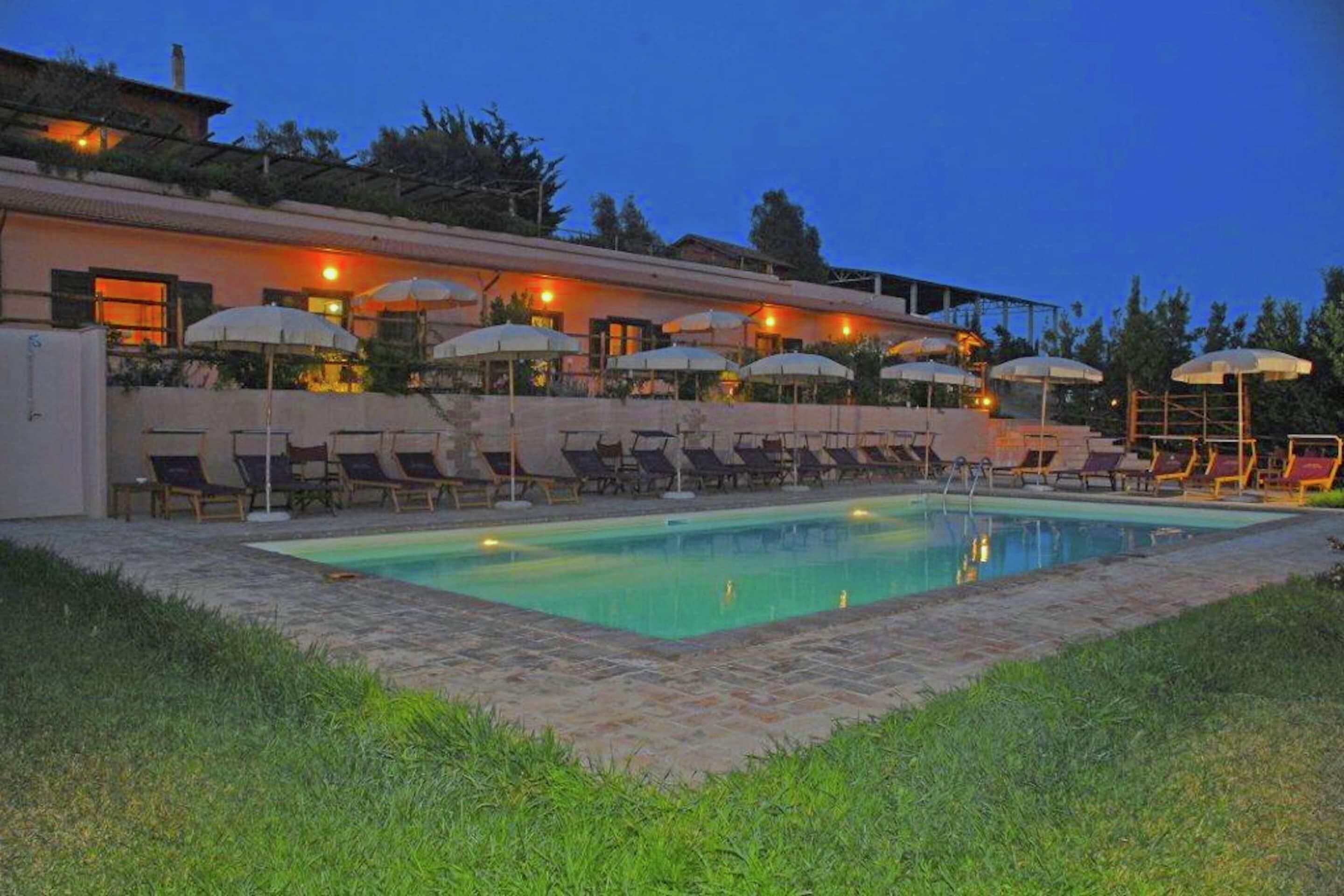 A pool area with lounge chairs and umbrellas, a building with a flat roof, and a clear sky.