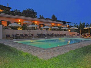 Un espace aménagé au bord de la piscine, avec des chaises longues et des parasols, entouré d’un bâtiment doté d’une terrasse.