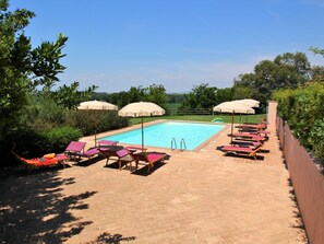 Une piscine entourée de verdure, avec des chaises longues et des parasols.