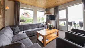 Un salón moderno con techo de madera, sofá gris, mesa de centro de madera y grandes ventanales que ofrecen vistas al exterior.