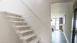 Eine moderne Treppe mit weißen Stufen führt zu einem Raum mit einem großen Fenster und Blick ins Freie.