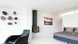 Ein modernes Wohnzimmer mit Kamin, einer Couch, einem Sessel und einem an der Wand hängenden Kunstwerk.
