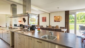 Une cuisine moderne dotée d’un grand îlot central, d’appareils électroménagers en acier inoxydable et offrant une vue sur la terrasse extérieure.