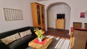 A living room with a black sofa, a wooden cabinet, a TV on a wooden stand, wicker chairs, and a red rug. - Your vacation home between forest and waves (Kellenhusen)