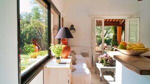 A room with a bed, a small table with a lamp, a window with a view of greenery, and a fruit bowl on a counter. - Holiday Home in Frejus Near Sea and Lake (Fréjus)