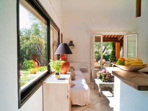 A room with a bed, a small table with a lamp, a window with a view of greenery, and a fruit bowl on a counter. - Holiday Home in Frejus Near Sea and Lake (Fréjus)